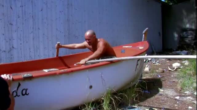 Bald muscular man rowing red and white boat outdoors